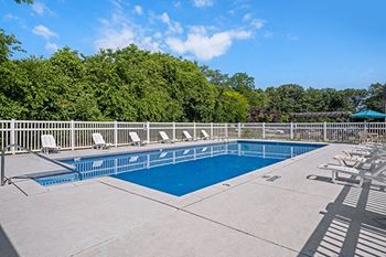 a swimming pool with deck chairs and trees in the background